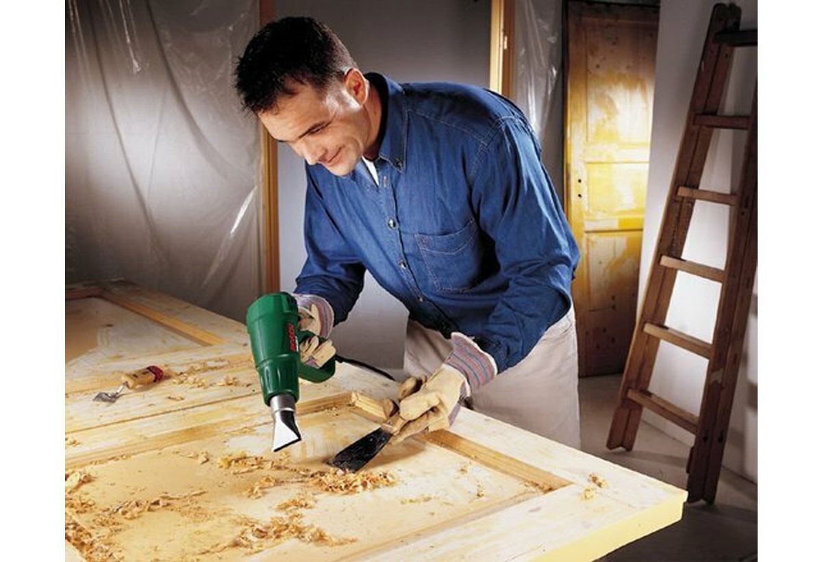 Απεικονίζεται η χρήση του πιστολιού για αφαίρεση βερνικιού από ξύλινη επιφάνεια.